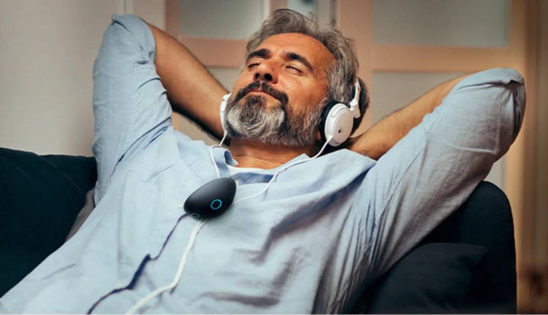 man wearing a sensate device on his chet comfotably relaxing with eyes closed hands behind his head with headphones